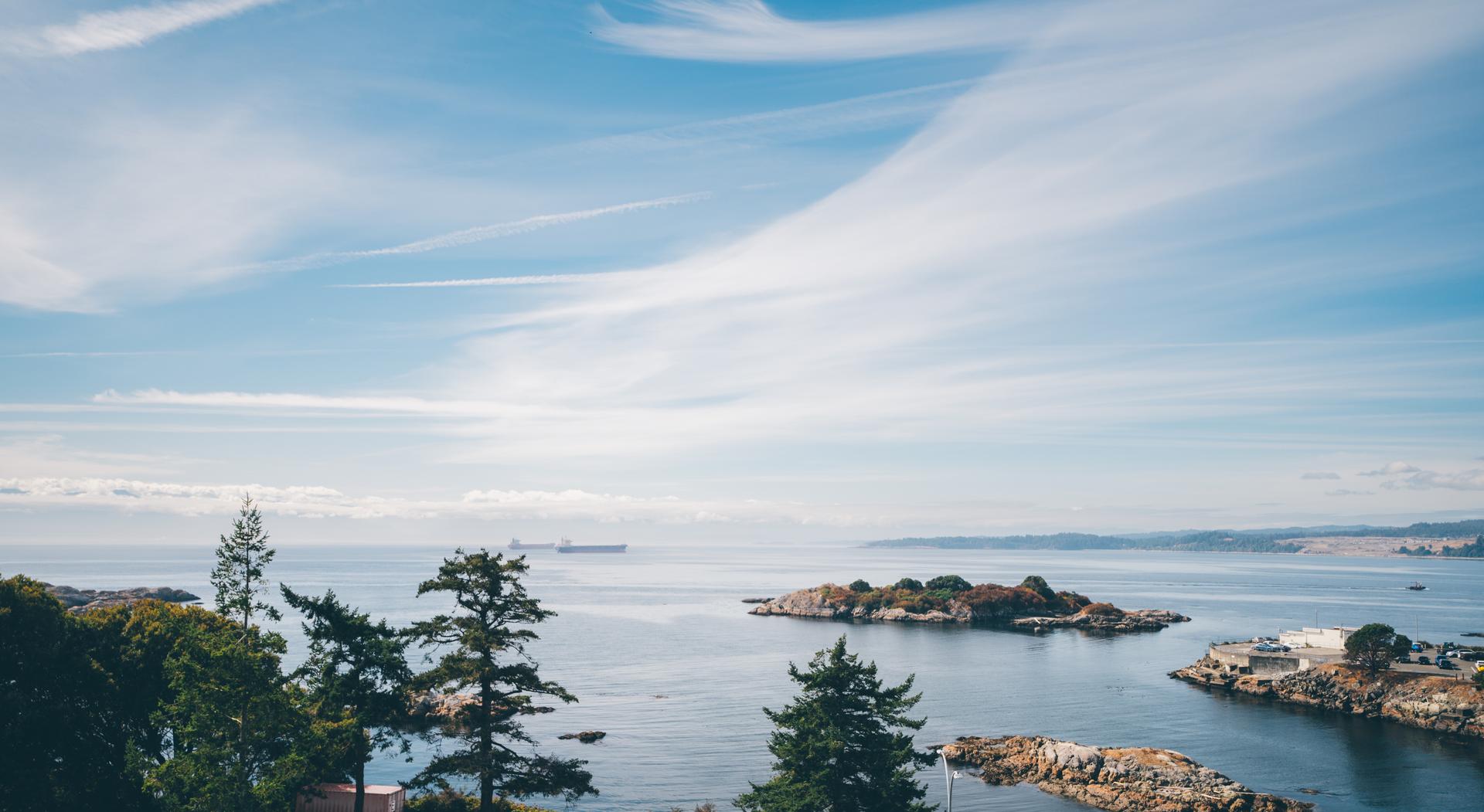 A coastal view of Victoria, British Columbia, with islands, trees, and ships under a blue sky.