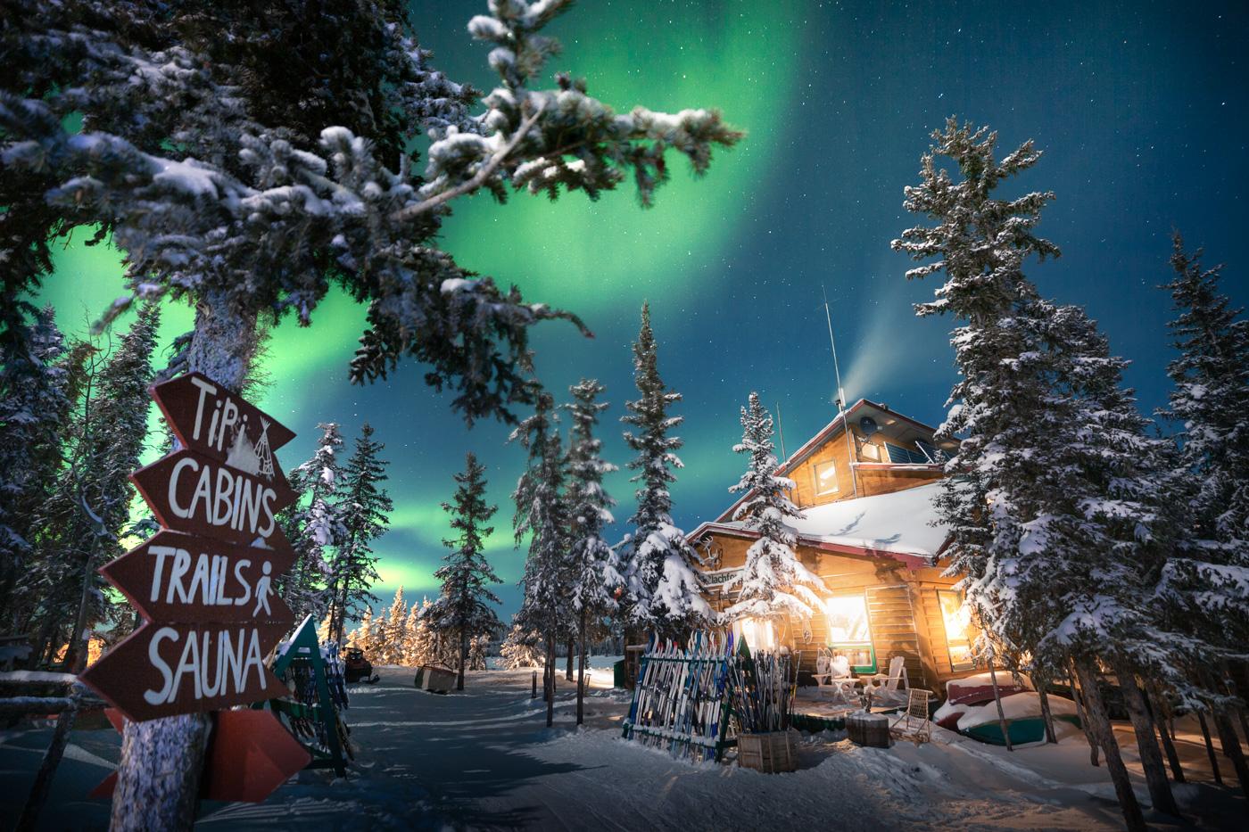 Blachford Lodge under the northern lights, surrounded by snowy trees at night