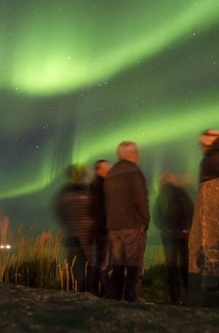 People gathered under the northern lights, next to an Inukshuk